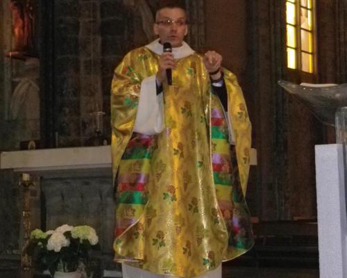 Le père José Van Oost revêtu d'une belle chasuble dorée parsemée de roses et de grappes de raisins.